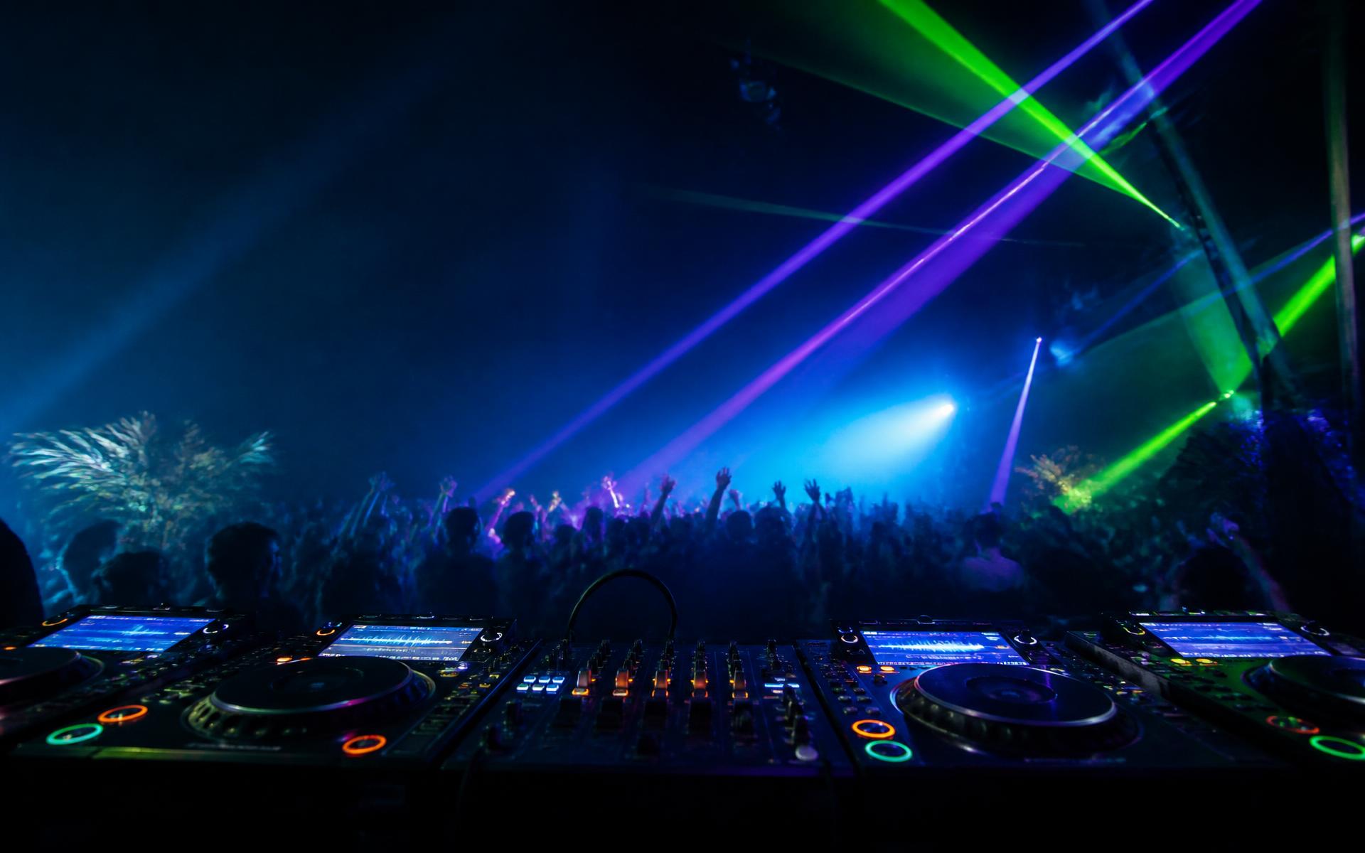 DJ booth overlooking a crowd beneath green and purple lasers